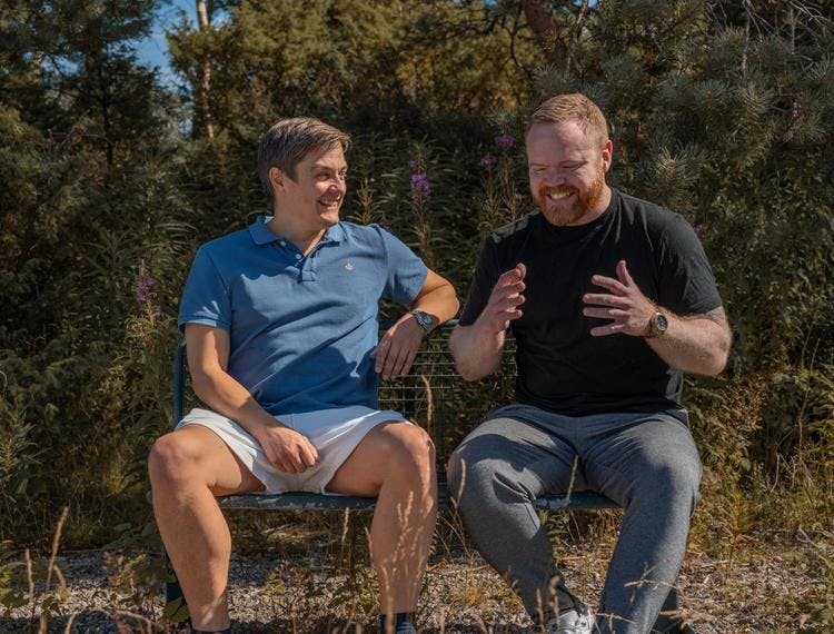 Bilde av programlederne for Åpne Forhold, Kyrre Dyregrov og André Clausen, som sitter på en benk og prater. 
