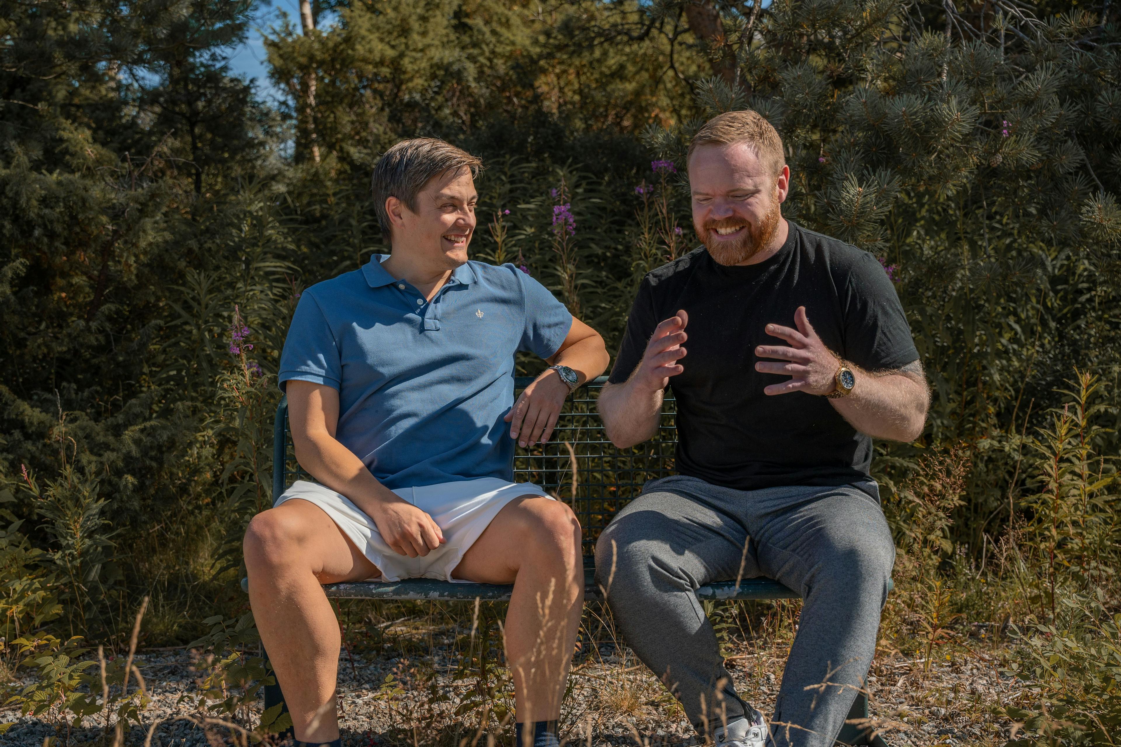 Bilde av programlederne for Åpne Forhold, Kyrre Dyregrov og André Clausen, som sitter på en benk og prater. 