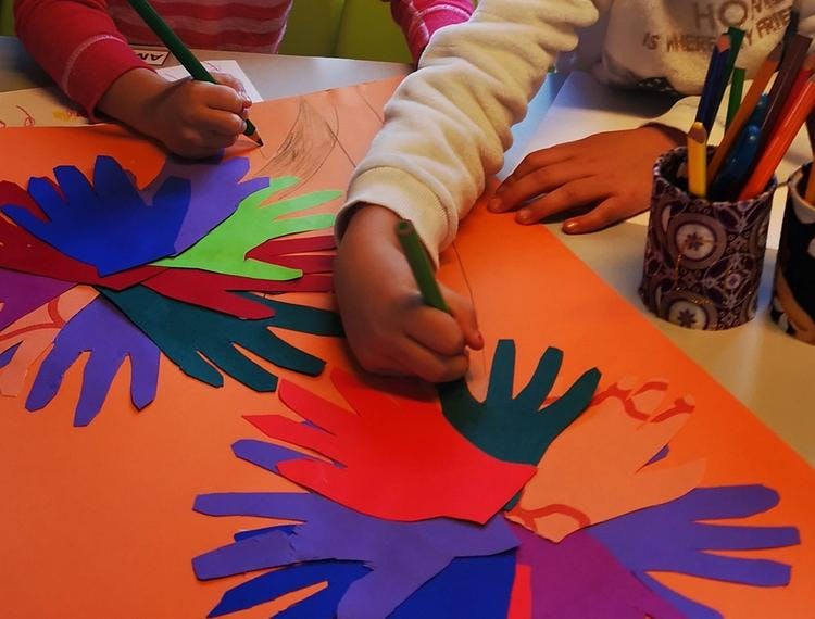 Bilde av barnehender som tegner på en plakat med mange hender på.