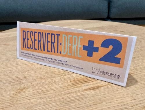 Foto av reservasjonskort på et bord. På kortet står det: "Reservert: Dere + 2". 